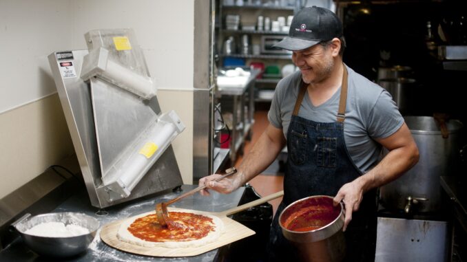 Joshua Garcia puts sauce on pizza in kitchen of his catering business.