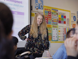 Polina Trask, a woman with long blonde hair and a black blouse with a multi-colored pattern, teaches in her adult education classroom.