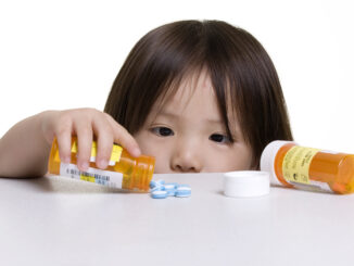 A child pours out several blue pills from a medication bottle onto a high counter top.