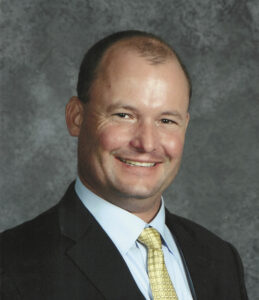 A professional photo of John Werner, Sequoia Adult Education Consortium Head, a smiling man in a black suit