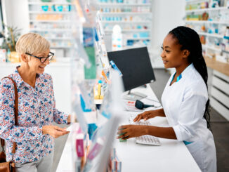 A smiling white senior woman buying medication from a young smiling black female pharmacist at a pharmacy