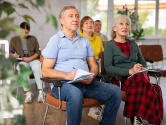Group of mature adults listening to someone speak in a room while taking notes