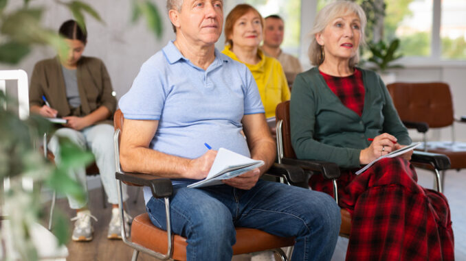 Group of mature adults listening to someone speak in a room while taking notes