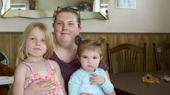 Destiny Wade-Pelkey sits in her home with her two young children in her lap