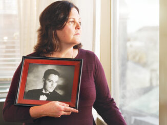 Sandra Chavez looking out a window while holding a senior portrait of her son Jeff Chavez.