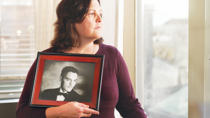 Sandra Chavez looking out a window while holding a senior portrait of her son Jeff Chavez.