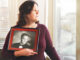 Sandra Chavez looking out a window while holding a senior portrait of her son Jeff Chavez.