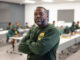 Jerry Irvin, a black man in a green long sleeved shirt, stands at his place of work with his arms crossed over his chest looking towards the camera