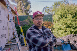 Photo of Jose Nunez in a plaid shirt and red ball cap with his arms crossed looking towards the camera