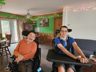 A photo of John Thompson on the left and Nick Mykytyn on right, both in motorized wheelchairs, at home with Christmas decorations in the background.