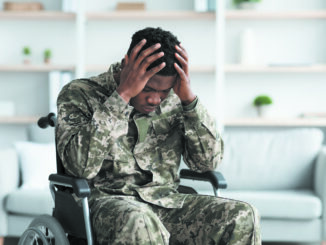 Upset black man sitting in wheelchair, wearing military uniform