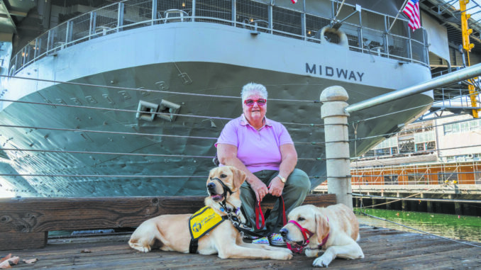 Portrait of Navy veteran Jude Litzenberger with her dogs Gunner, at left, and Archer near the USS Midway Museum at San Diego Bay.