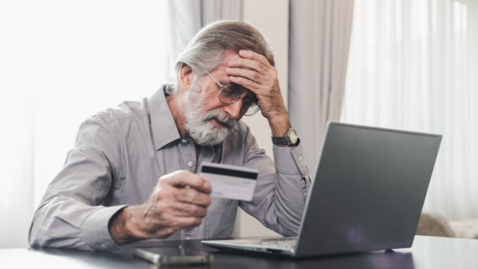 Upset senior elderly man holding credit card by laptop having trouble worry finance safety data or online payment security.