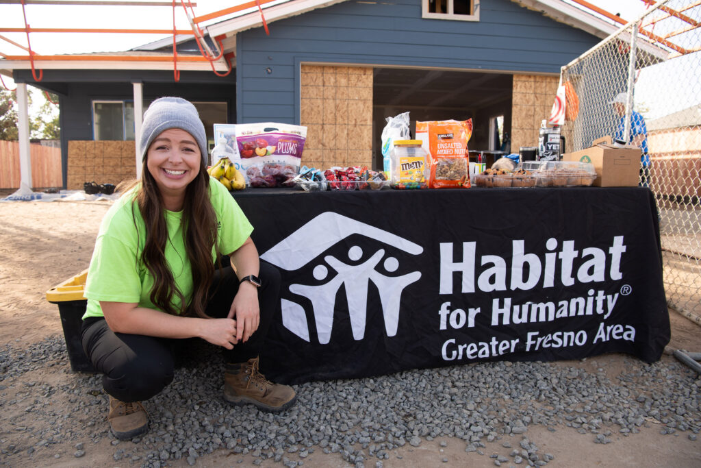 Celena Genest crouching in front of a Habitat for Humanity sign