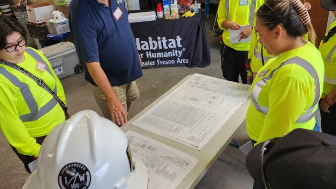 Rick O’Daniel, in a blue shirt, speaks to several people in high visibility work clothing