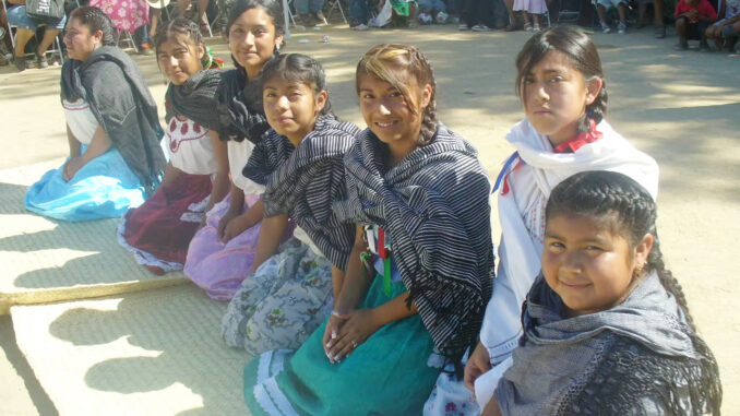 OES_S13_Flood_Unidad Popular Benito Juarez_Todec_01 A photo of seven girls in traditional Mexican outfits sitting in the middle of a crowd at an event