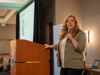 Angelique Ashby at a podium speaking into a microphone