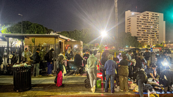 A small crowd of homeless and low-income individuals gathered at night with Down But Not Out employees