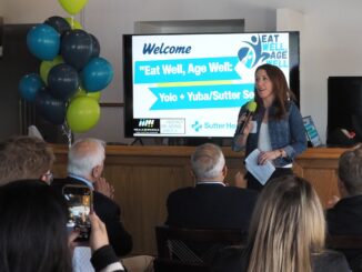 A group of people watching a woman give a presentation with a large power point in the background.
