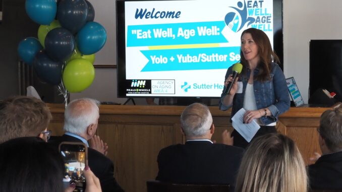 A group of people watching a woman give a presentation with a large power point in the background.