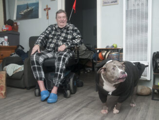 Man sitting in a chair in his home with his dog beside him.