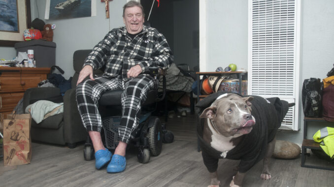 Man sitting in a chair in his home with his dog beside him.