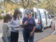 A group of people all looking at a clipboard while standing in front of a Meals on Wheels delivery van.