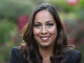 A portrait of a woman smiling with foliage in the background.