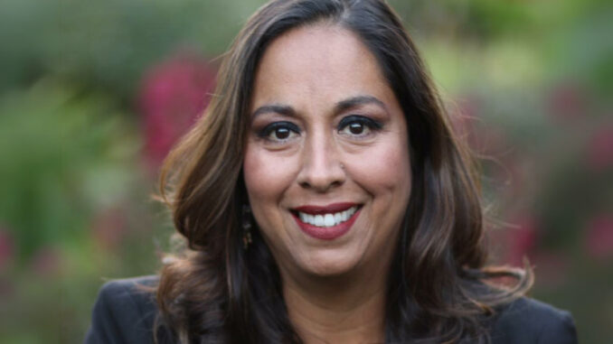 A portrait of a woman smiling with foliage in the background.