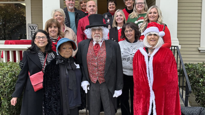 A group of Meals on Wheels volunteers dressing in Christmas caroling costumes standing on the front porch of a house.