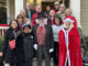 A group of Meals on Wheels volunteers dressing in Christmas caroling costumes standing on the front porch of a house.
