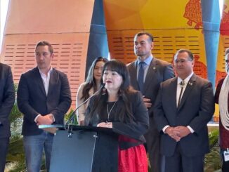 A photo at speaking at a podium with several people standing behind her.