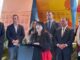 A photo at speaking at a podium with several people standing behind her.