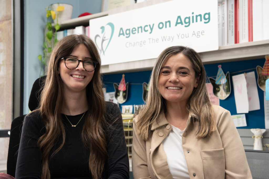 Two women standing next to each other in a Agency on Aging office, smiling.