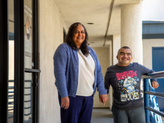A mother and her son, standing in a hallway, smiling.
