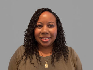 A portrait of a women smiling with a neutral grey background.