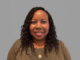A portrait of a women smiling with a neutral grey background.